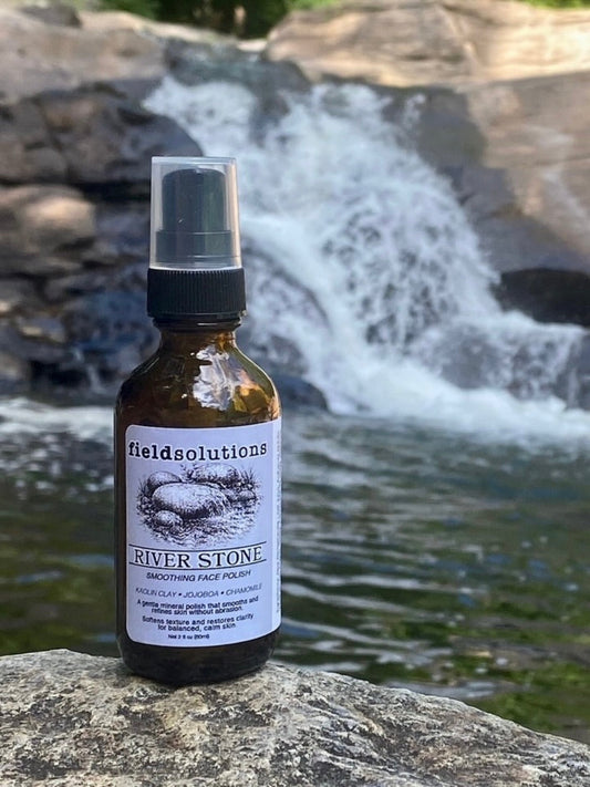 River Stone kaolin clay face polish in an amber glass pump bottle on a rock beside a waterfall