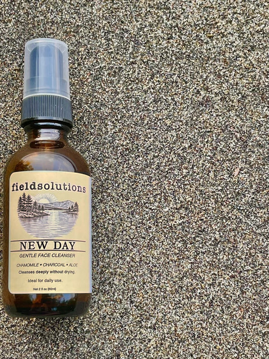 New Day gentle gel face cleanser in an amber glass pump bottle on sand